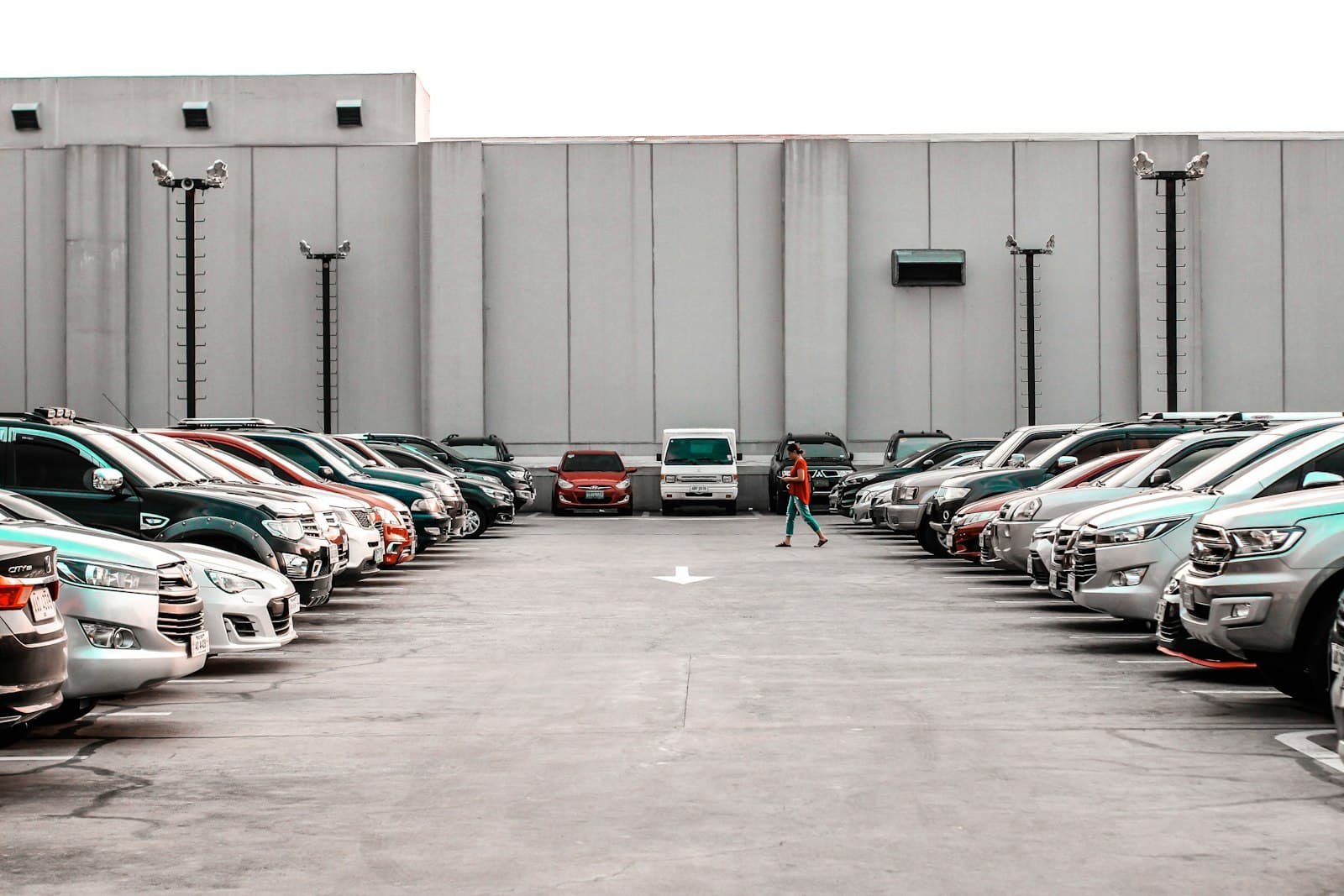 A person walking between two rows of cars on a lot