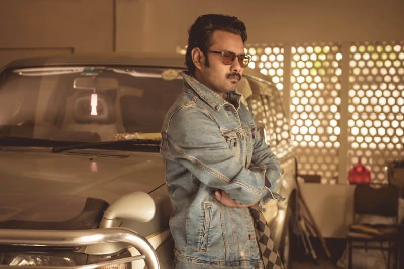 A man in a denim jacket leaning on a truck in the garage