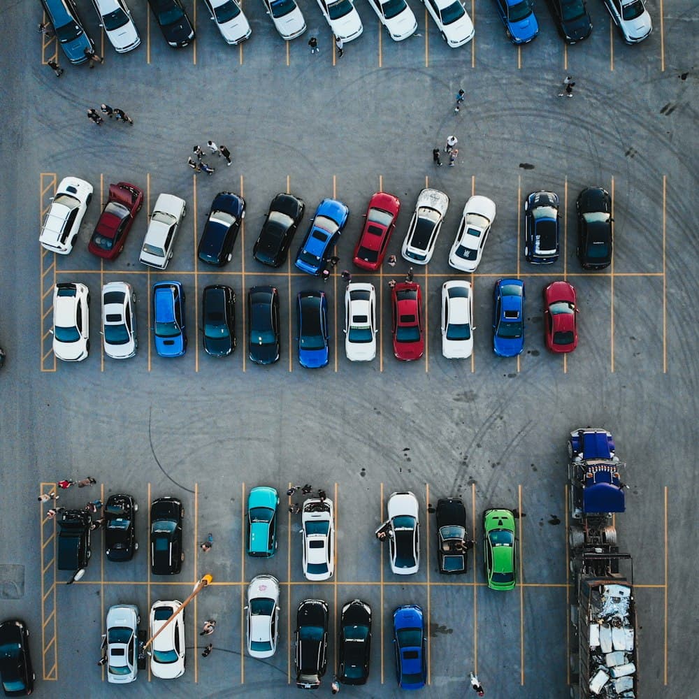 A car lot seen from above, staff working between the rows