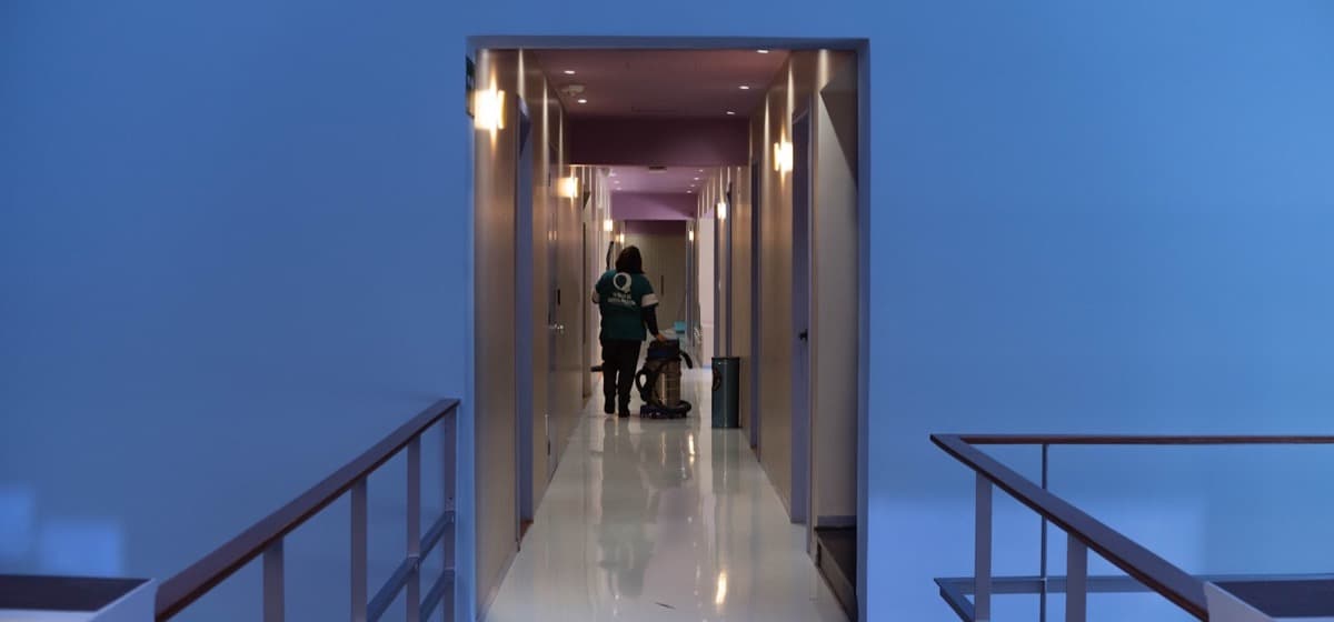 A cleaner working a quiet hallway with a vacuum in the evening