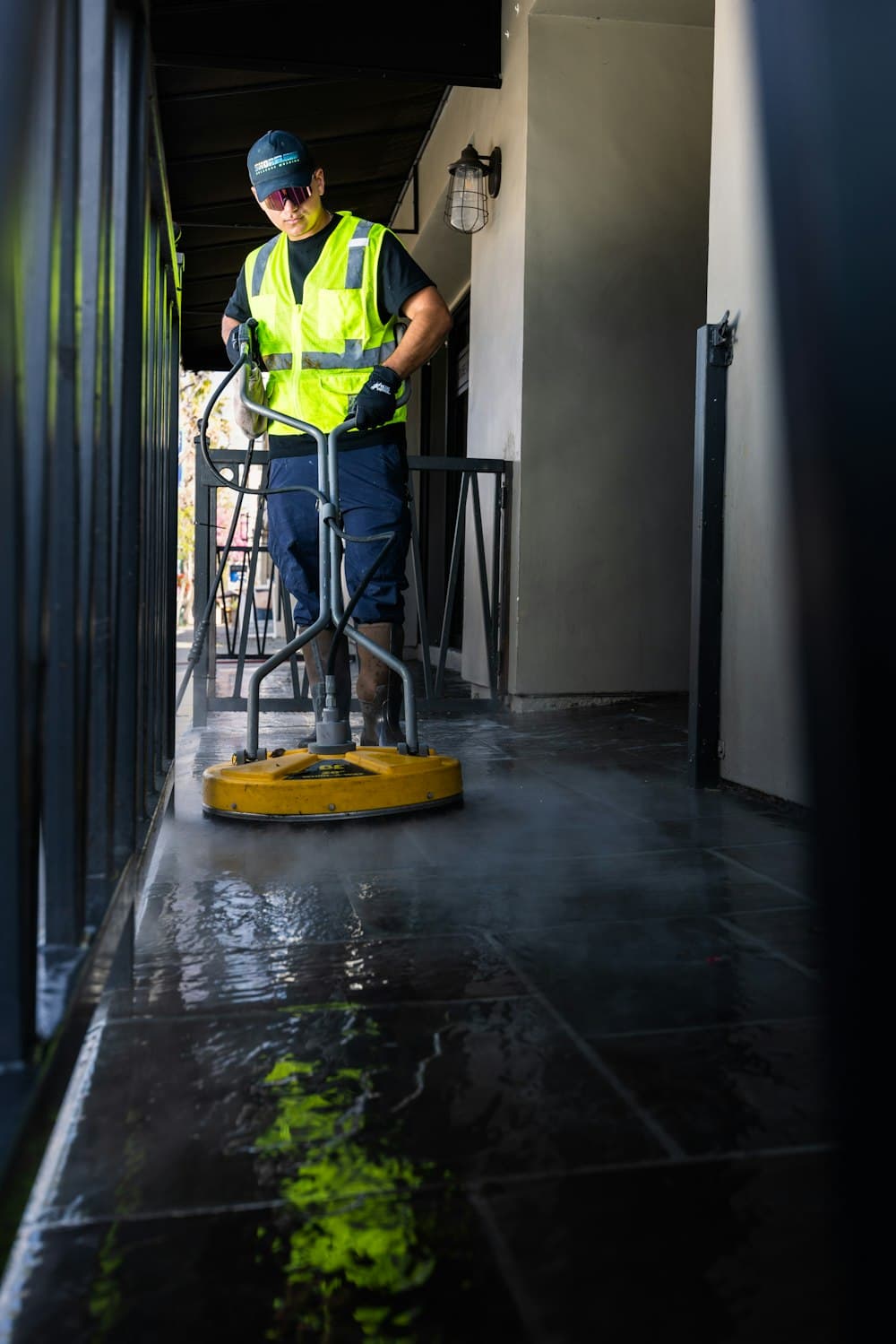 A worker in a safety vest pressure-washing a walkway
