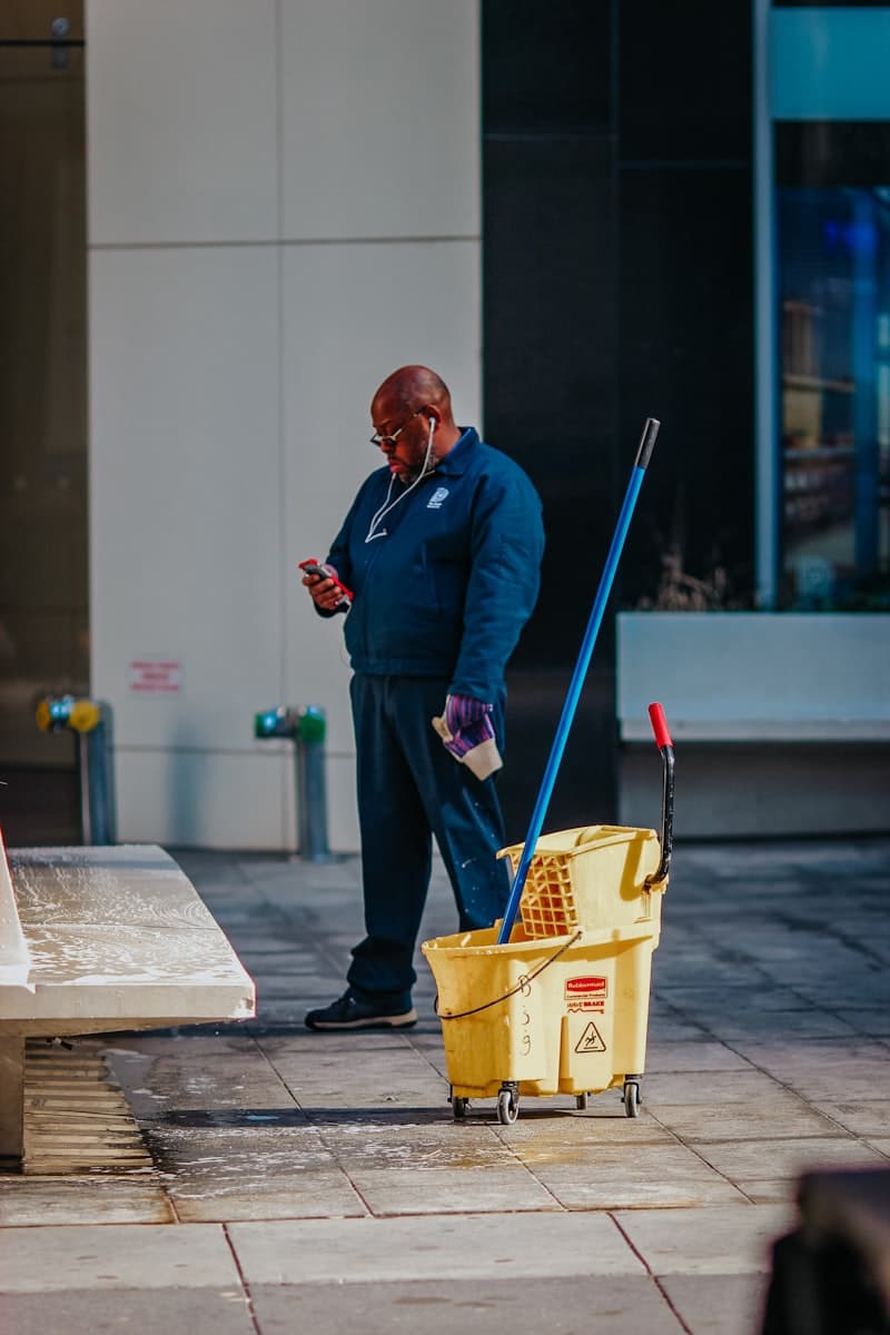 A man checking his phone beside a mop bucket outside a building