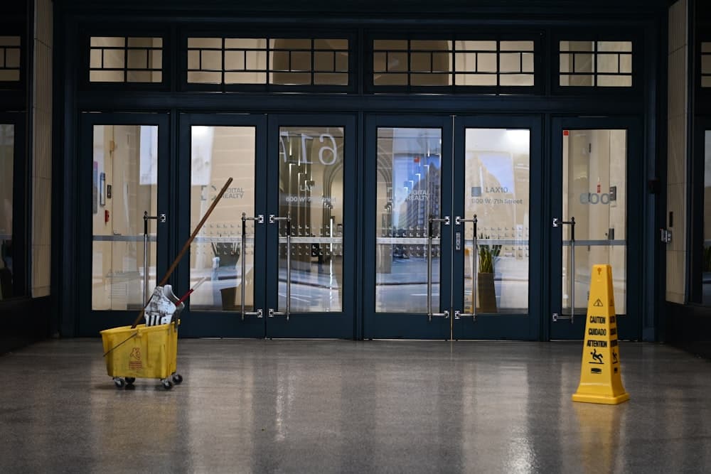 A mop bucket and caution cone in front of glass entrance doors