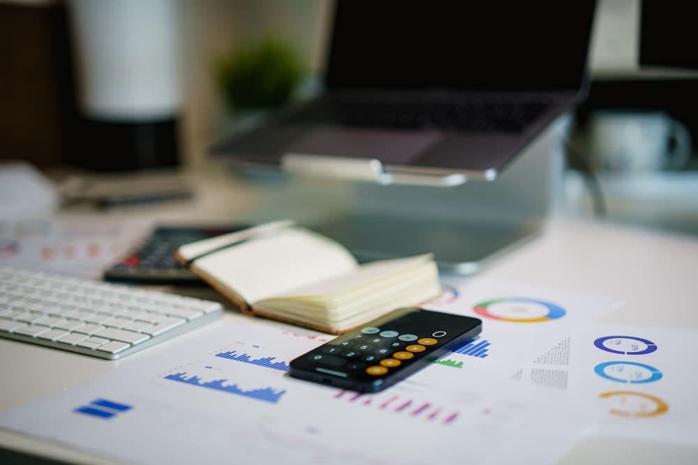 A desk with printed reports, a notebook, and a calculator app