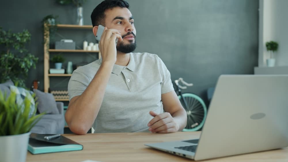 A man on the phone at his desk beside an open laptop