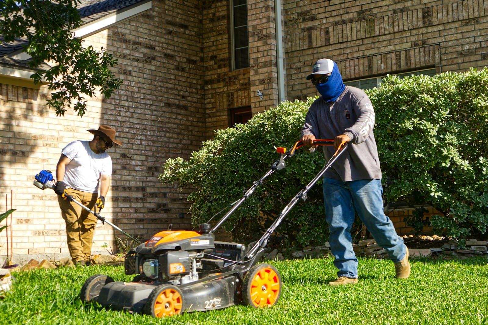 Two crew members mowing and trimming a residential lawn
