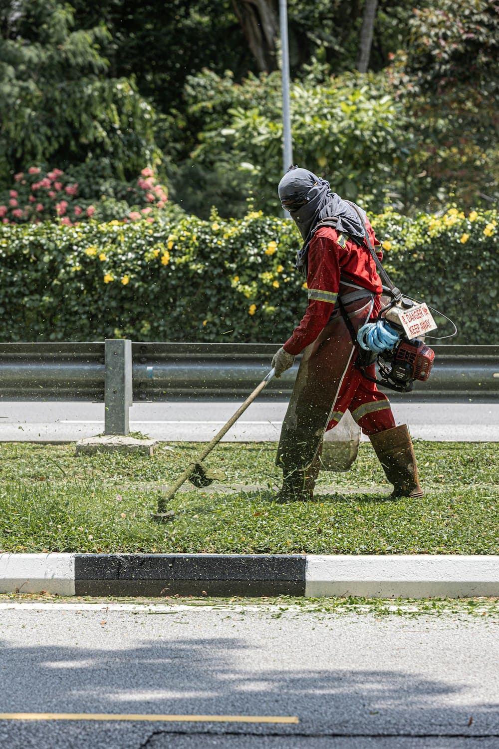 A worker trimming grass with a string trimmer