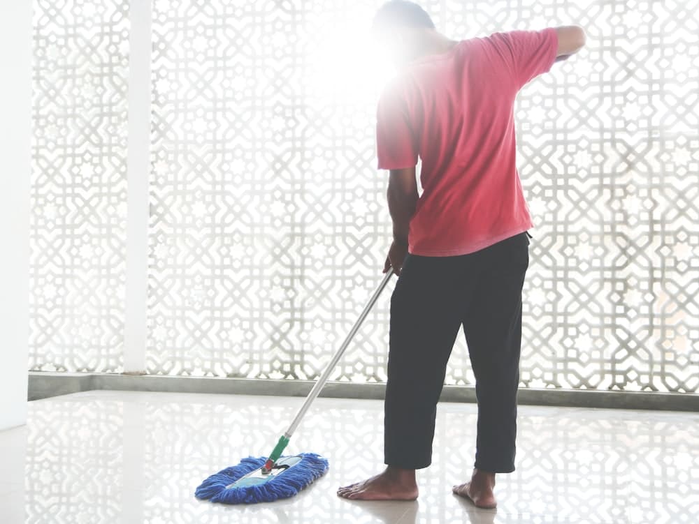 A person carrying a broom and cleaning bucket
