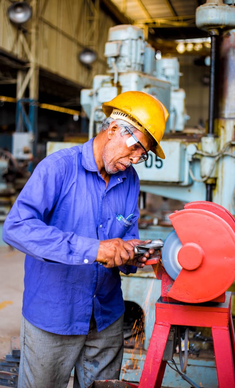 A man grinding a metal tool beside industrial machinery