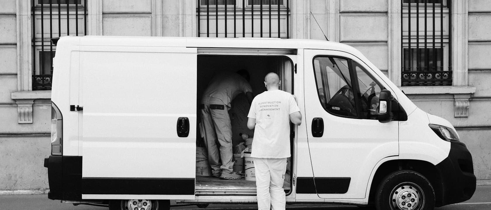 Two workers loading a white van parked on a city street