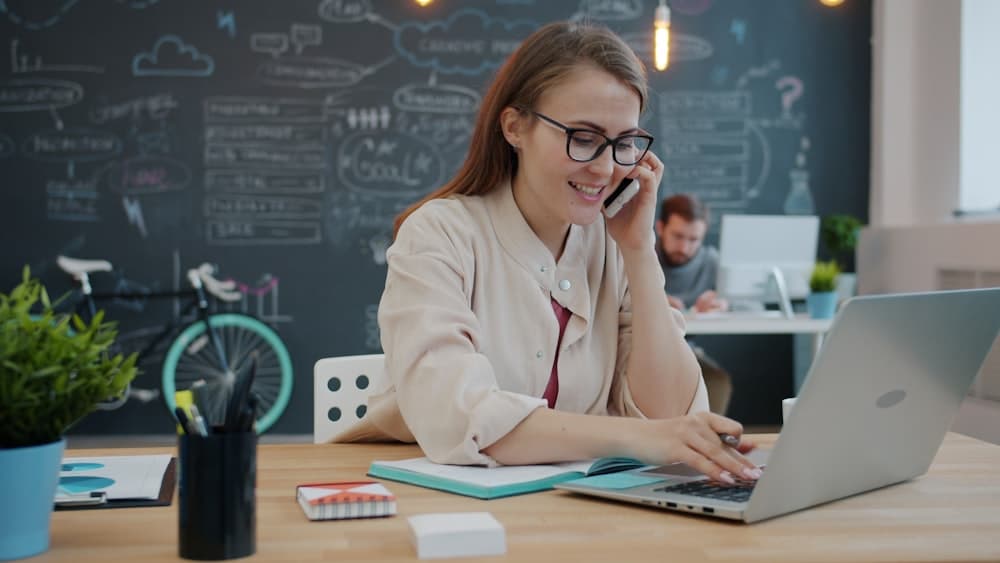 A person on the phone at an office desk with a laptop