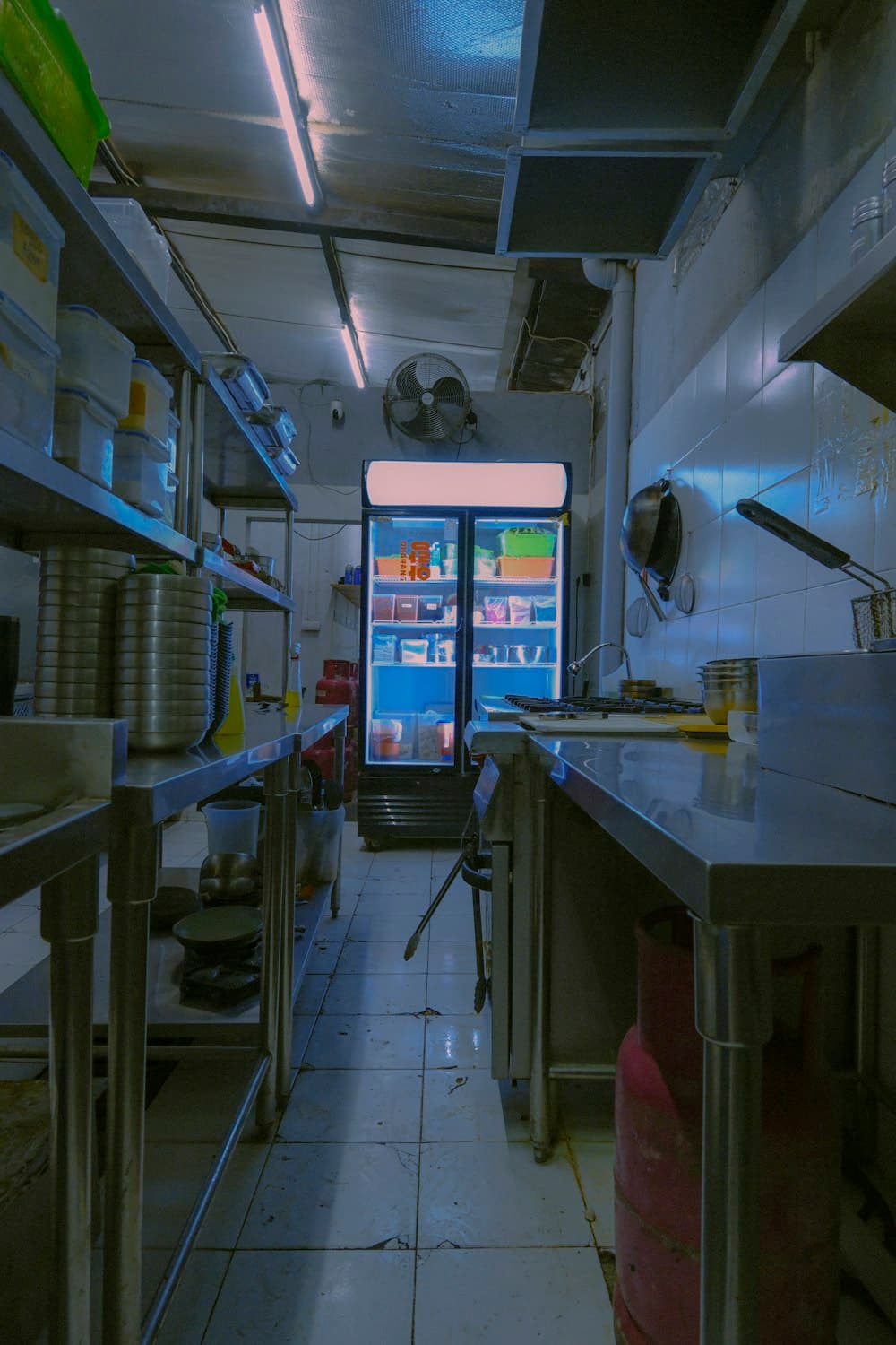 A narrow commercial kitchen with stainless steel prep tables