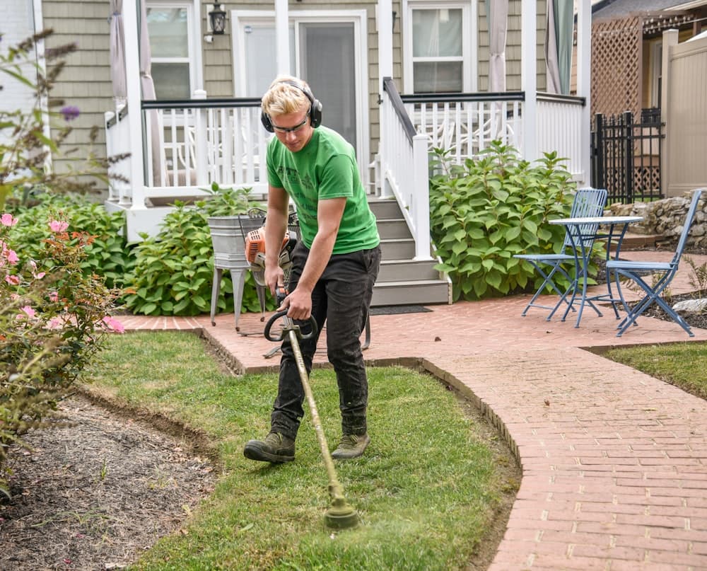 A landscaper in work clothes carrying a shovel
