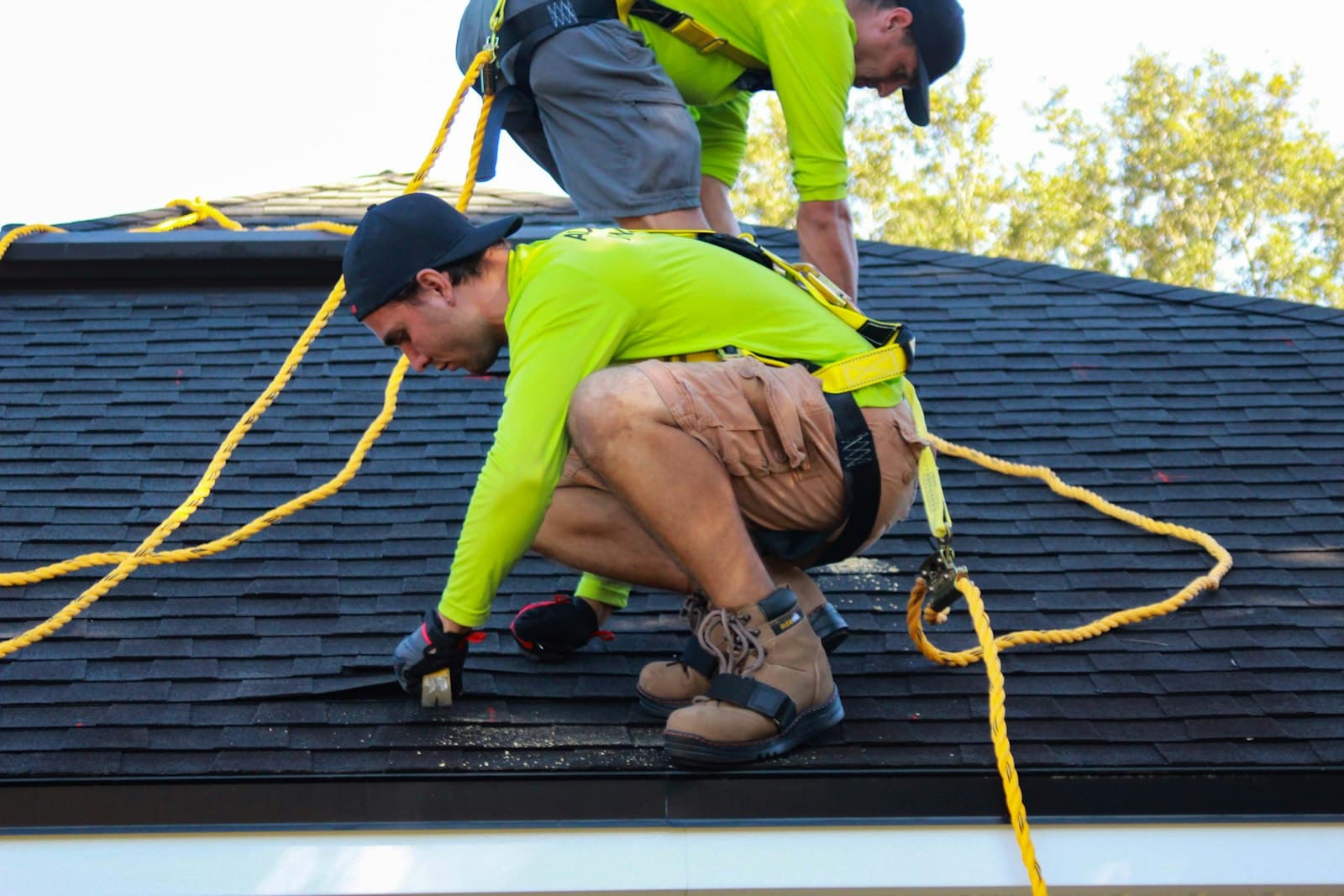 Two roofers in harnesses laying shingles on a steep roof