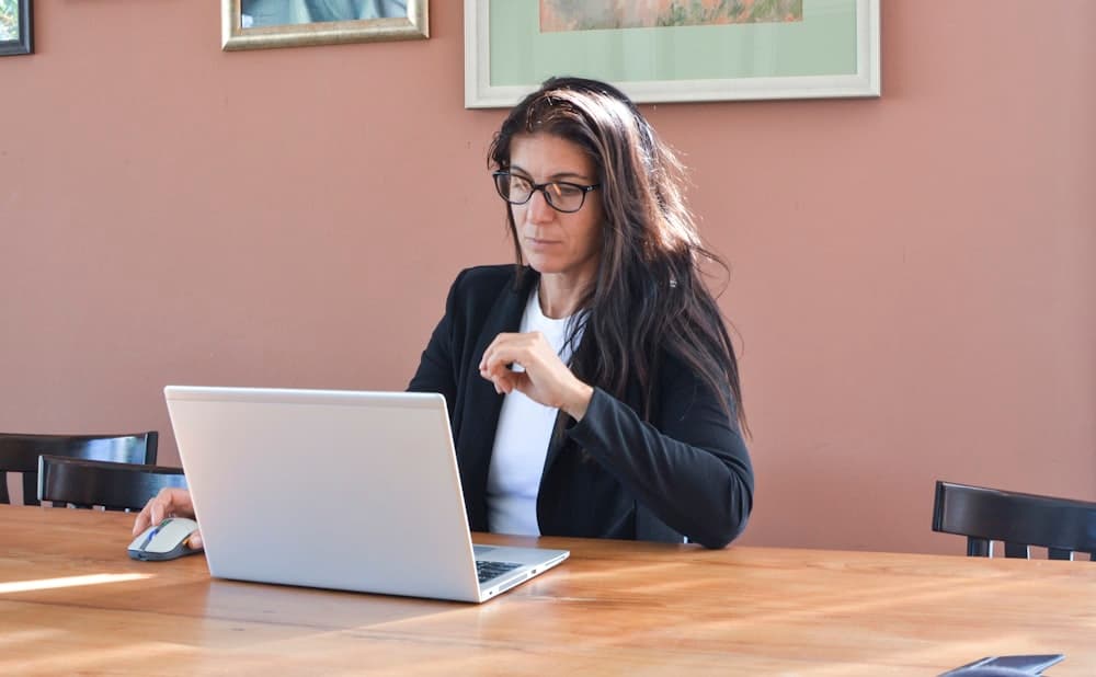 A woman in glasses working on a laptop at a table