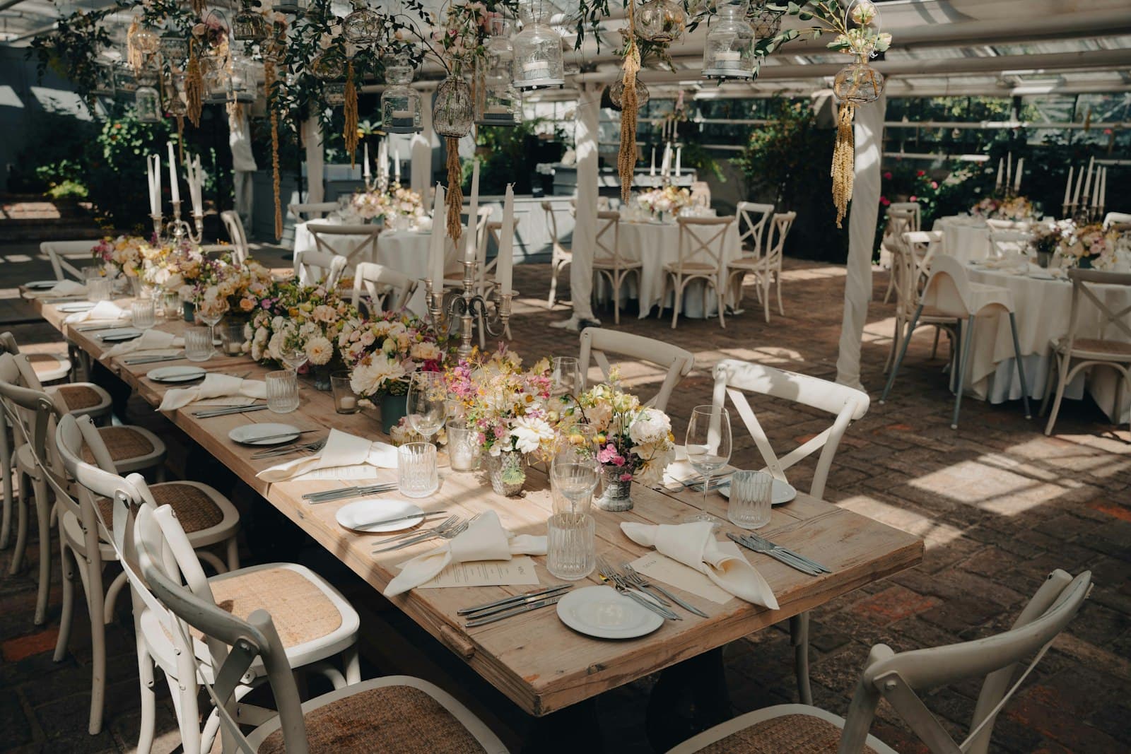 A garden room set for a wedding with long tables and hanging lanterns