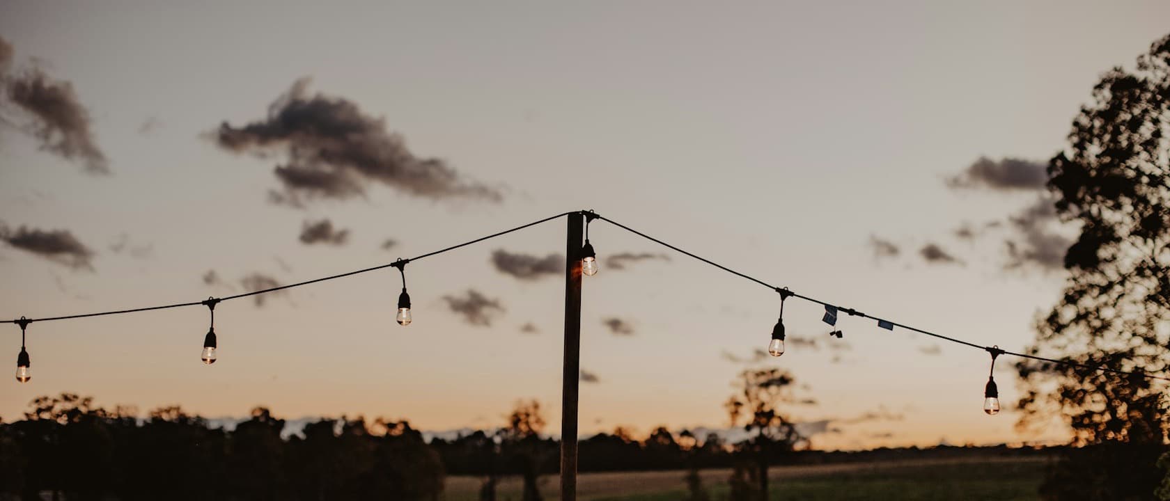 String lights over a field at dusk after the tables are cleared