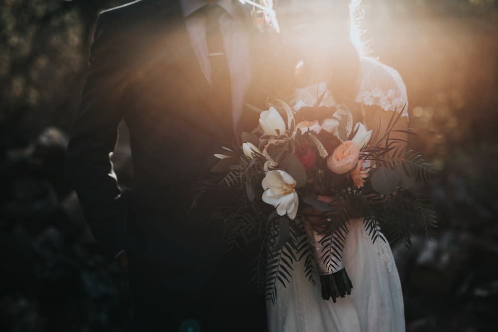 A couple holding a bouquet photographed against low sun
