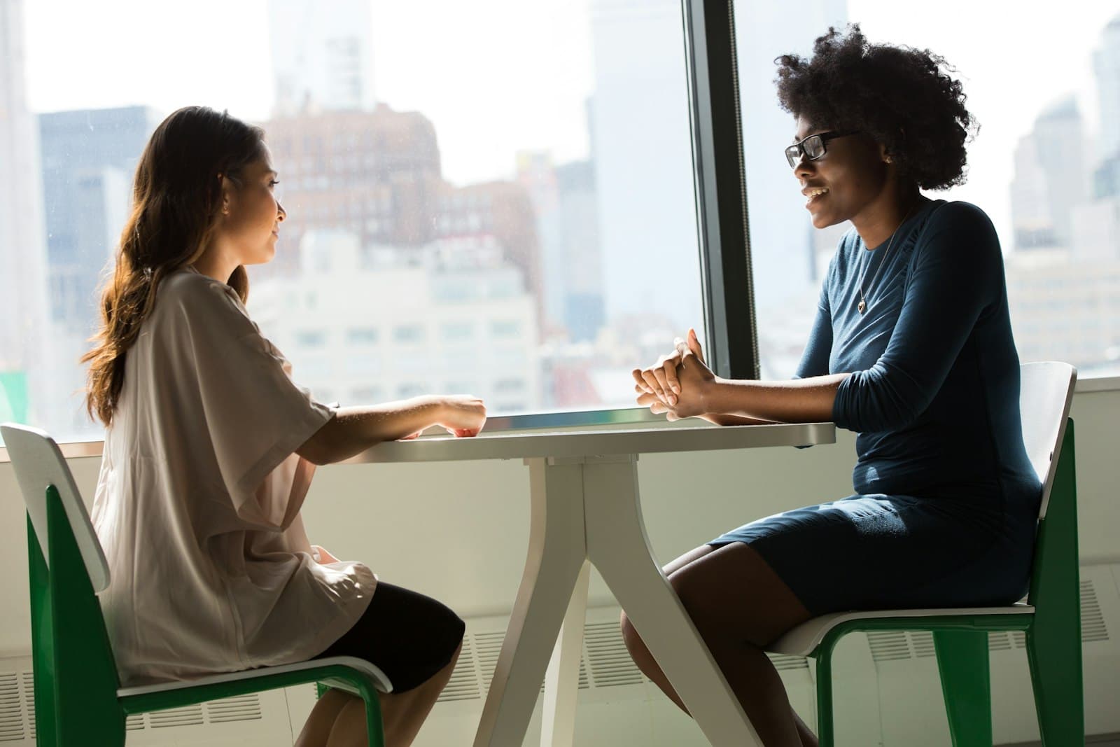 Two people in conversation across a small table by a window