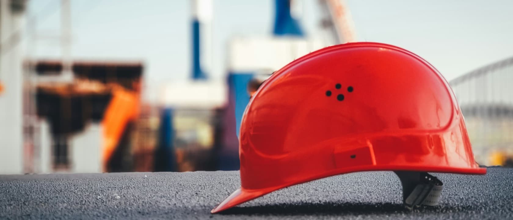 A hard hat resting on fresh asphalt with cranes behind