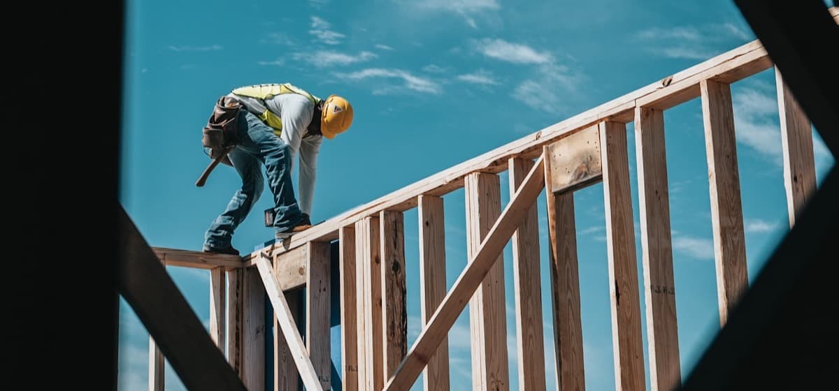 A framer working the top plate of a stud wall against the sky