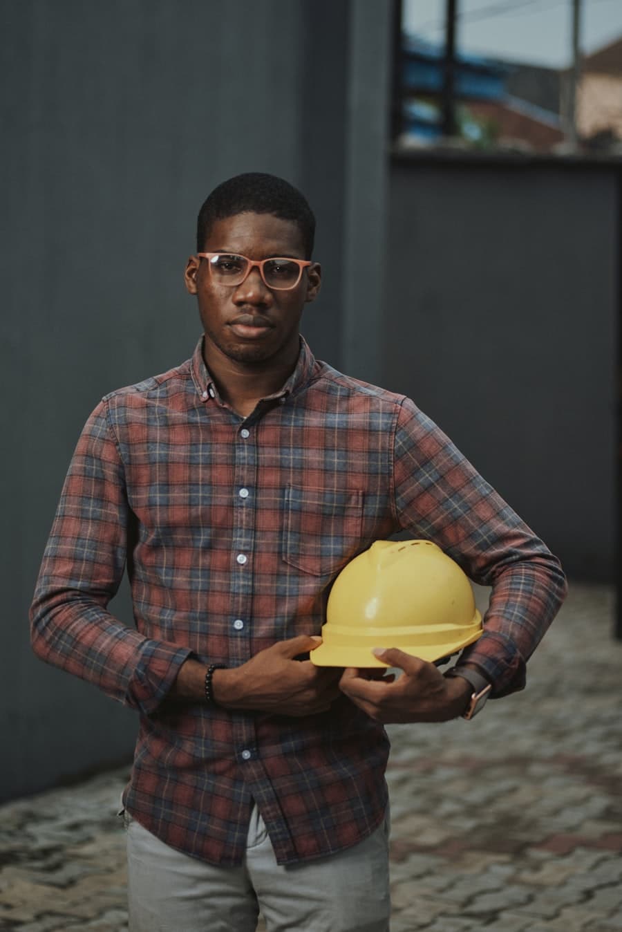 A young contractor holding a hard hat outside a site wall