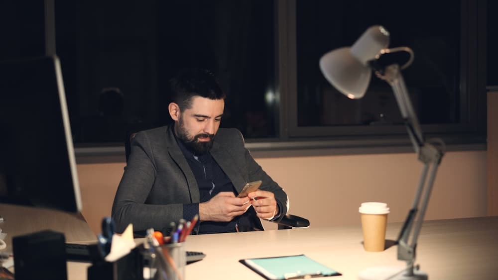 A man working late at a desk with his phone