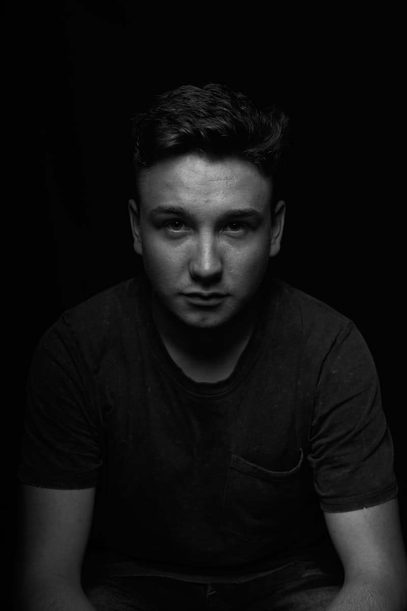 A man in a black t-shirt photographed against a plain wall