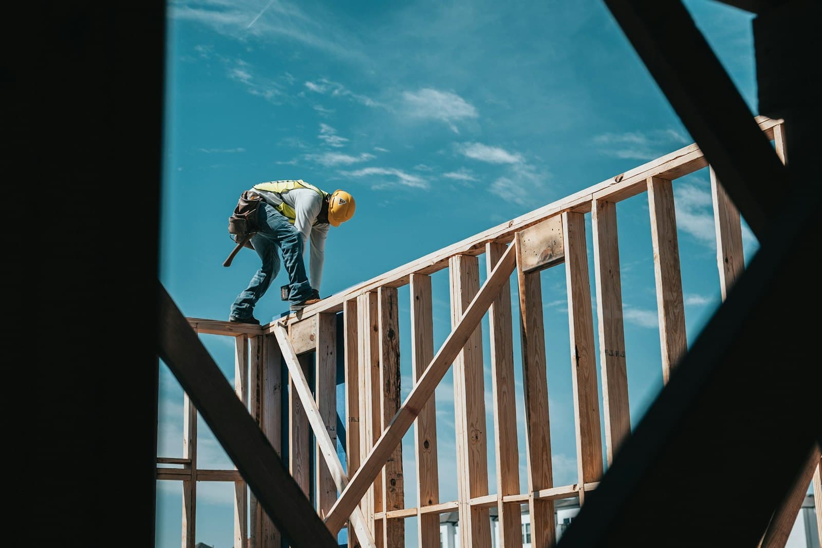 A framer walking the top plate of a wood-framed wall against the sky