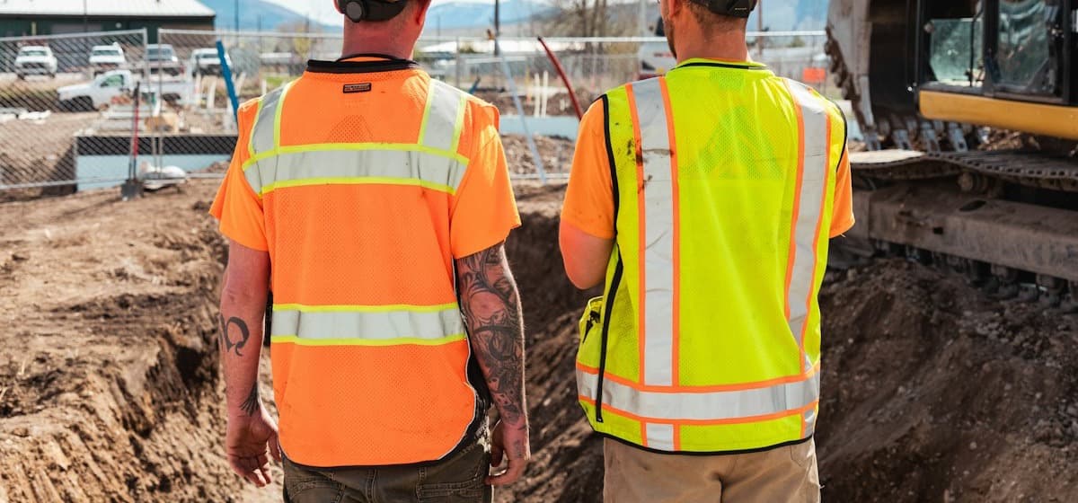 Two crew members in safety vests overlooking an excavation