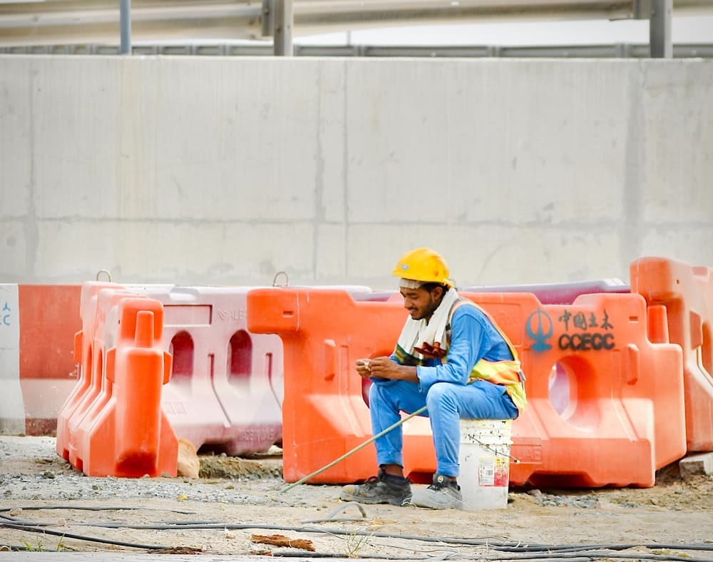 A worker sitting on a bucket at a site checking his phone