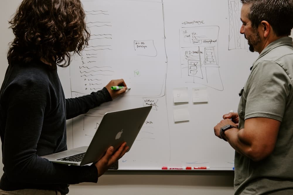 Two people pricing a job at a whiteboard with a laptop