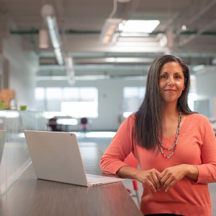 A woman standing at an office desk with a laptop