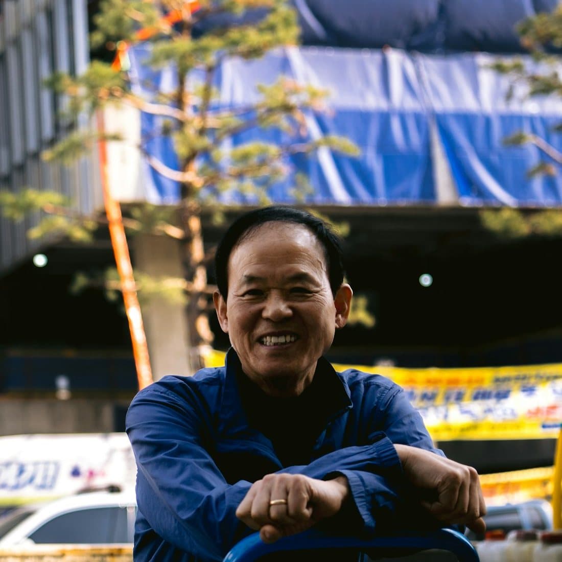An older tradesman in blue workwear smiling at a job site