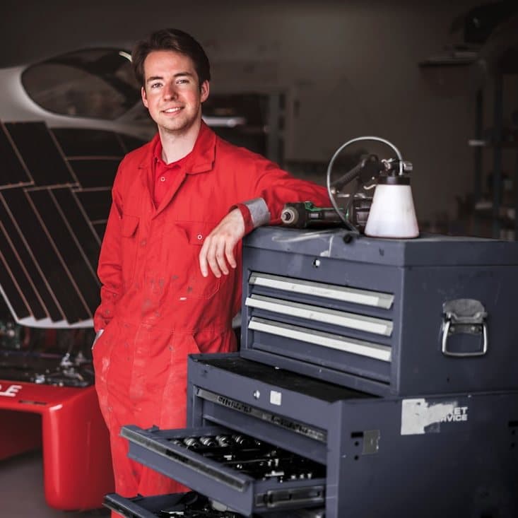 A technician in red coveralls beside a tool cart