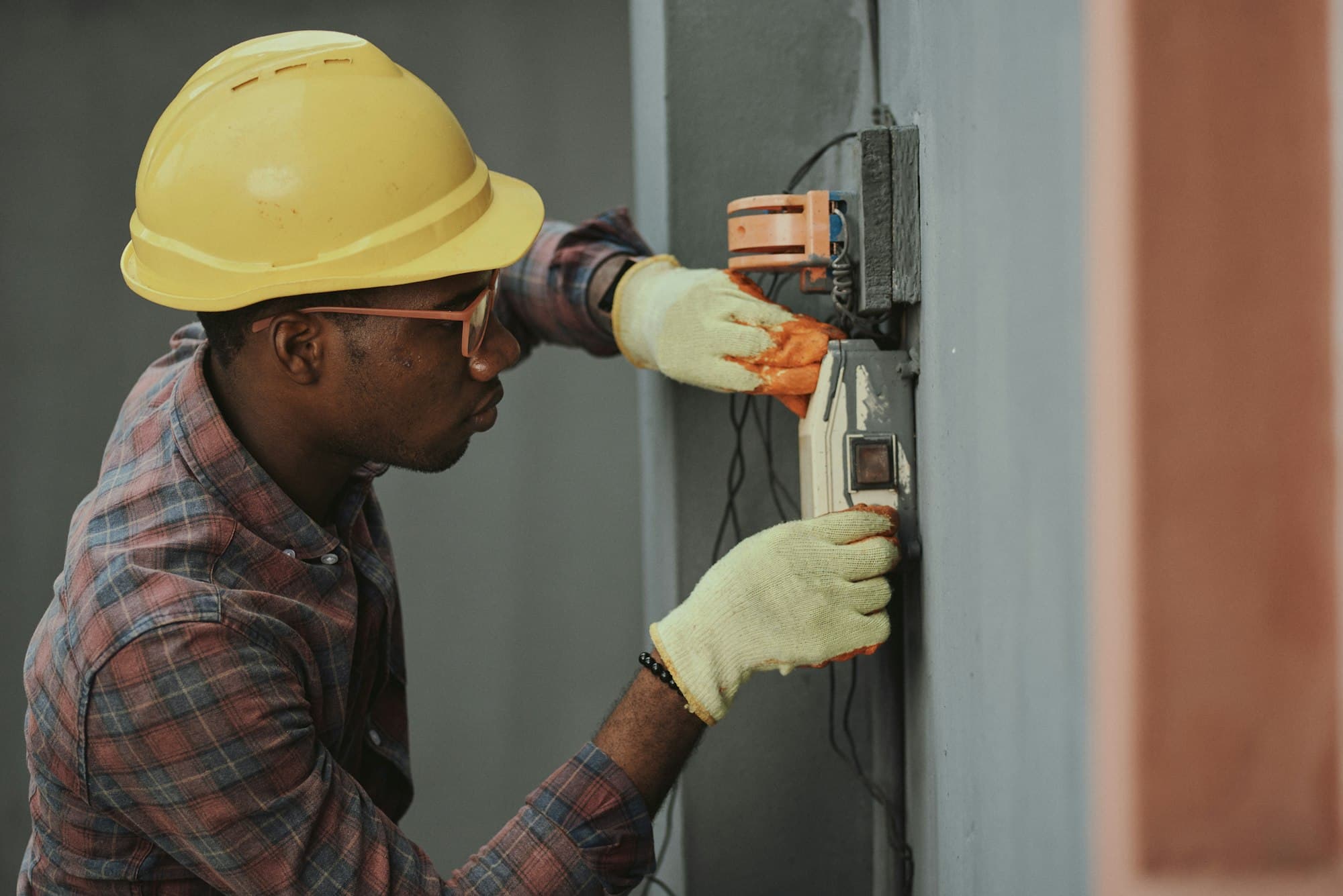 An electrician in a hard hat wiring a panel on site