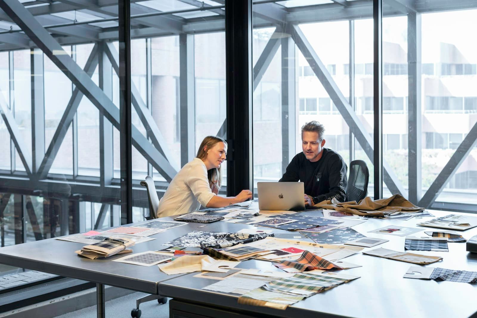 Two people reviewing material samples at a large worktable in a bright studio