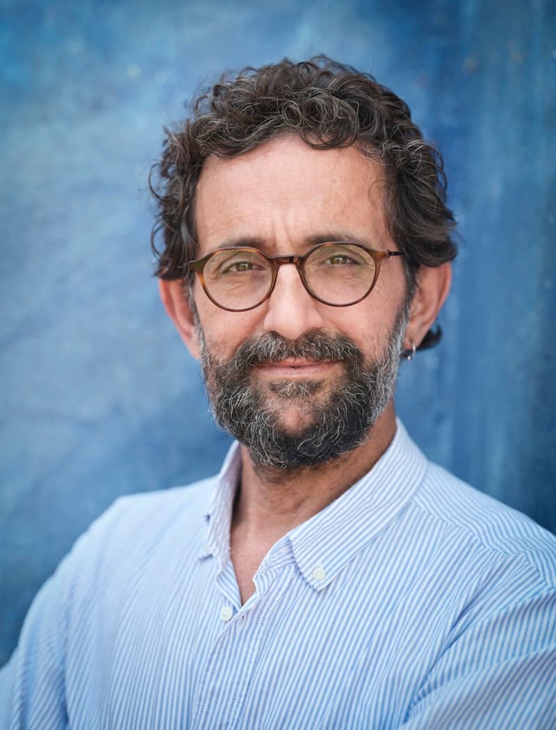 A bearded man with glasses in a light blue shirt