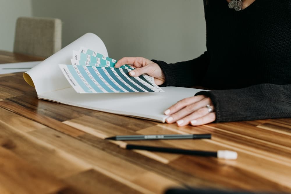 Hands presenting a fan of color swatches across a wooden desk