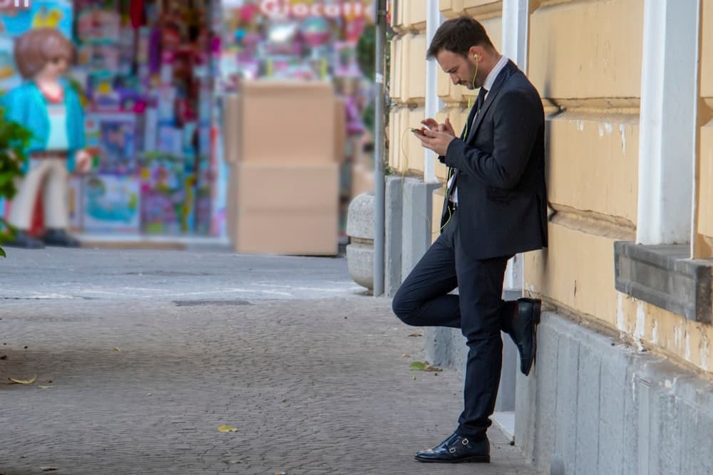 A man checking his phone while leaning on a building outside