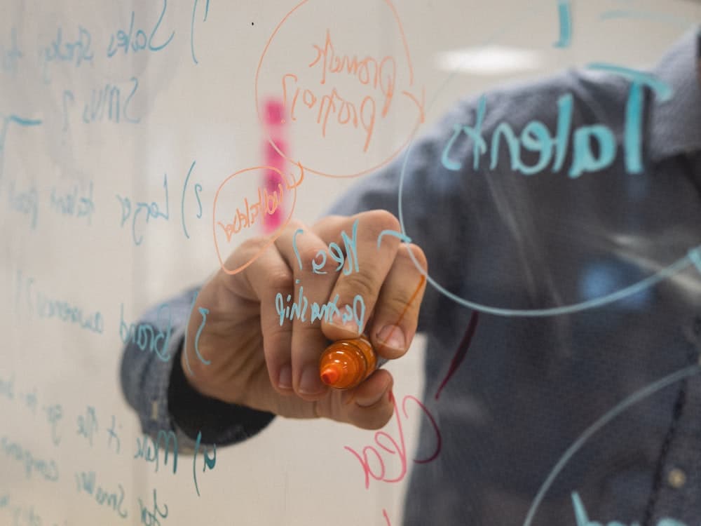 A consultant sketching diagrams on a glass whiteboard