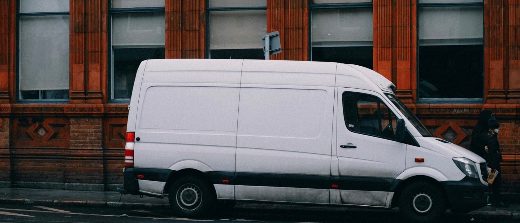 A white work van parked on the street outside a brick building