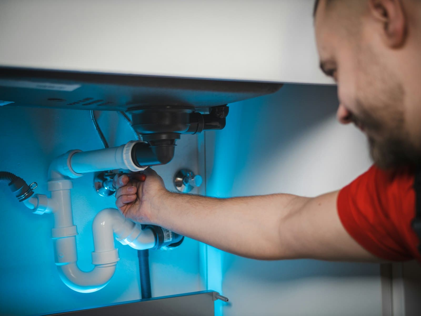 A plumber adjusting the trap and supply lines under a sink