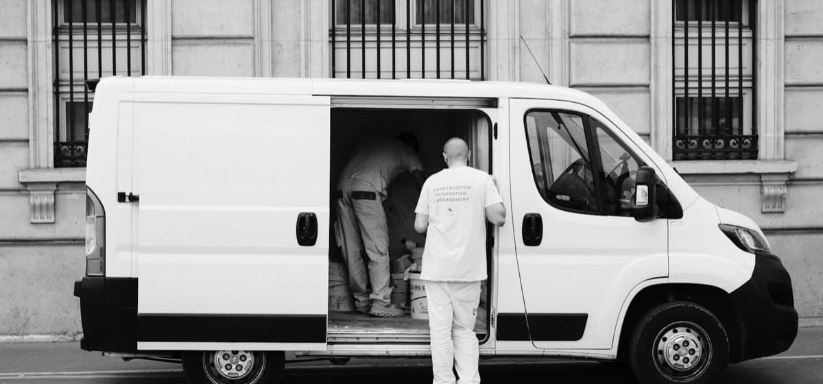 Two workers loading a panel van outside a city building