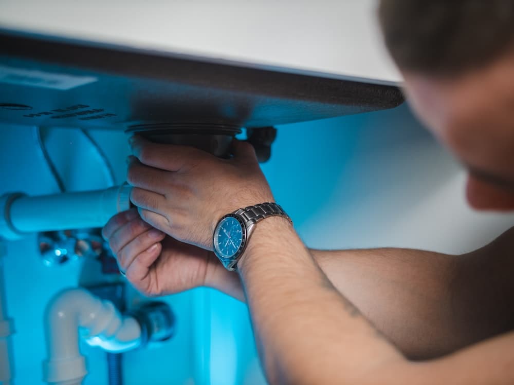 A plumber reaching into a sink cabinet to set a drain fitting