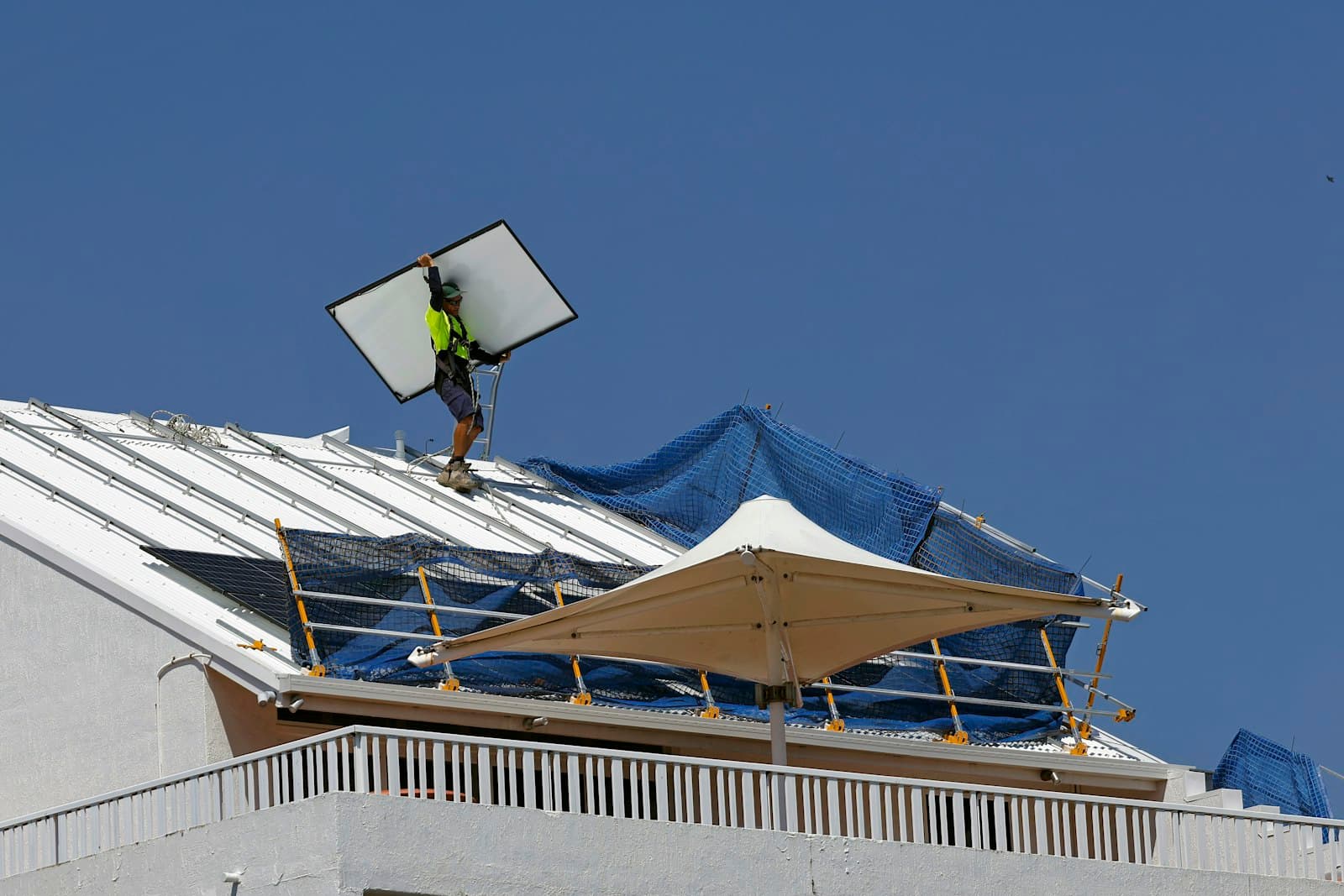 An installer carrying a solar panel up a residential roof