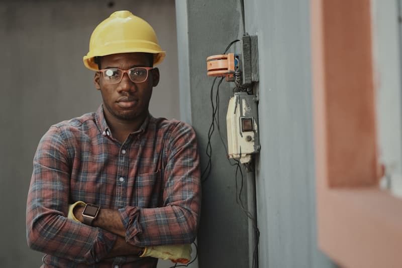A tradesman in a hard hat leaning against a site wall
