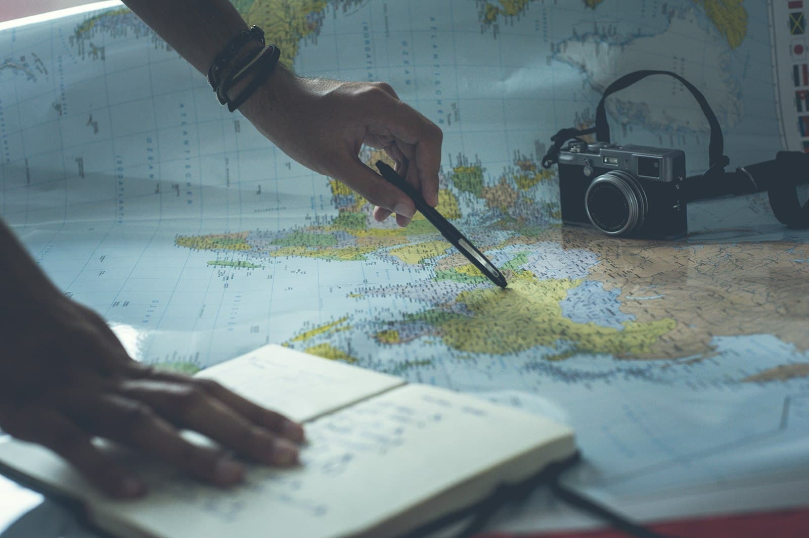 Hands tracing a route across a world map with a pen and notebook