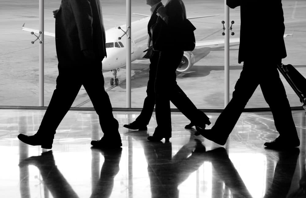 Silhouetted travelers walking a terminal past a parked aircraft