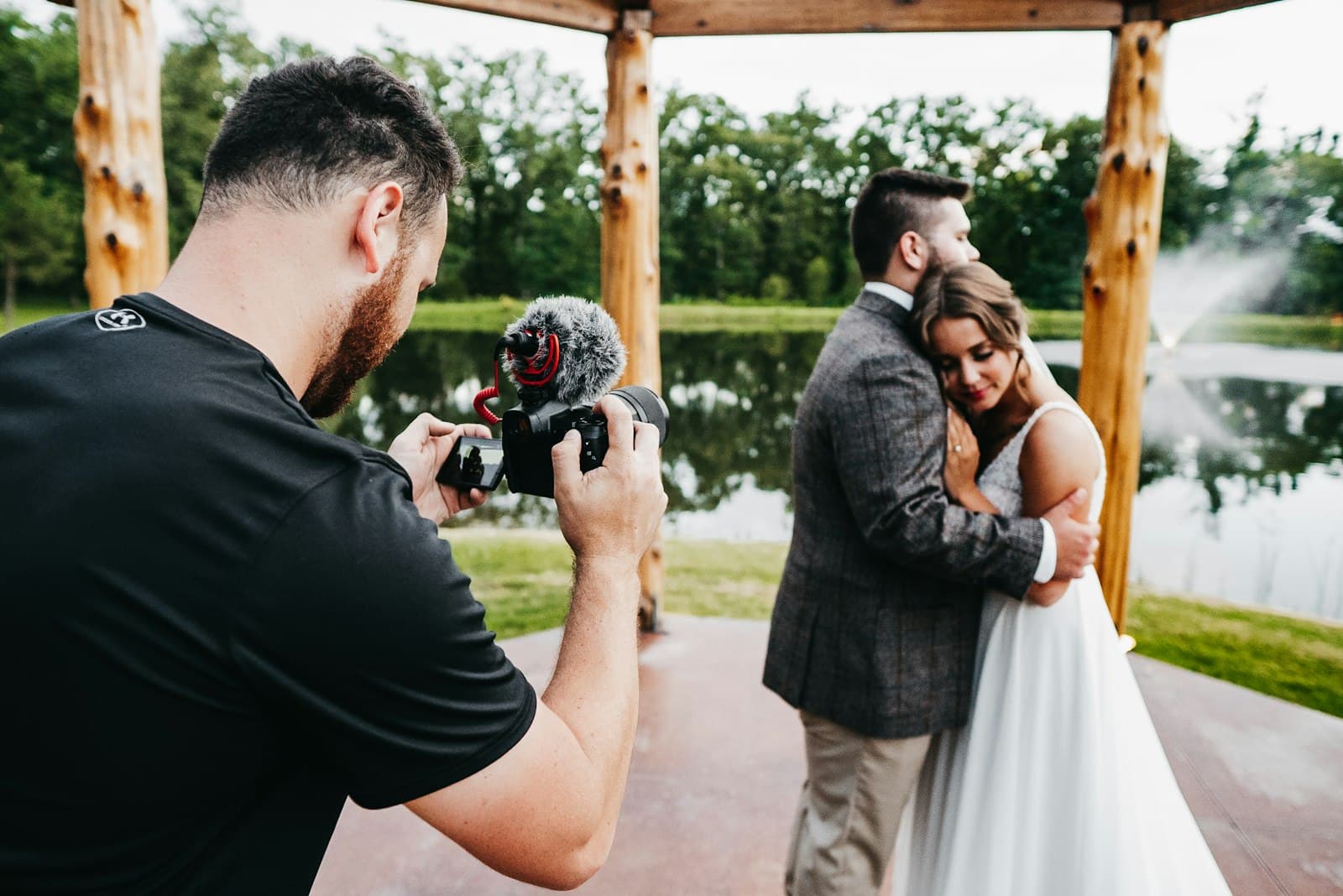 A videographer filming a couple with a gimbal rig at a lakeside venue